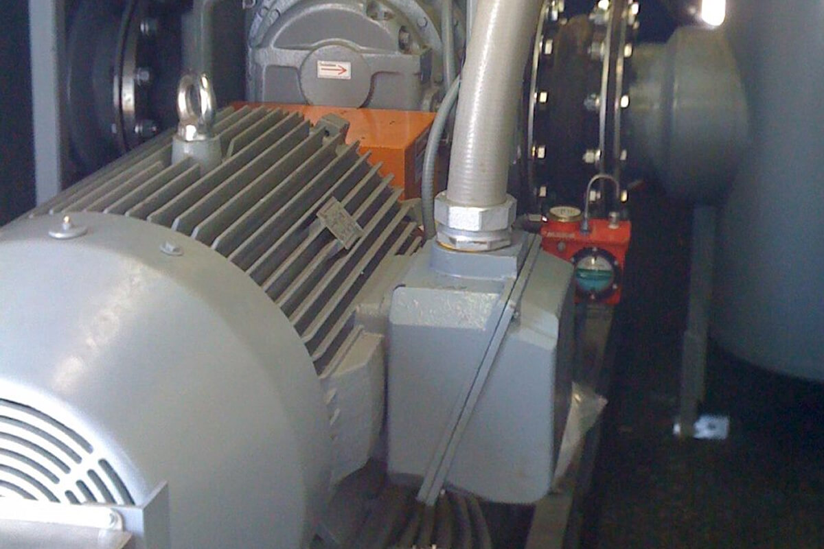 Close-up of an industrial electric motor connected to piping and mechanical components inside a processing system.